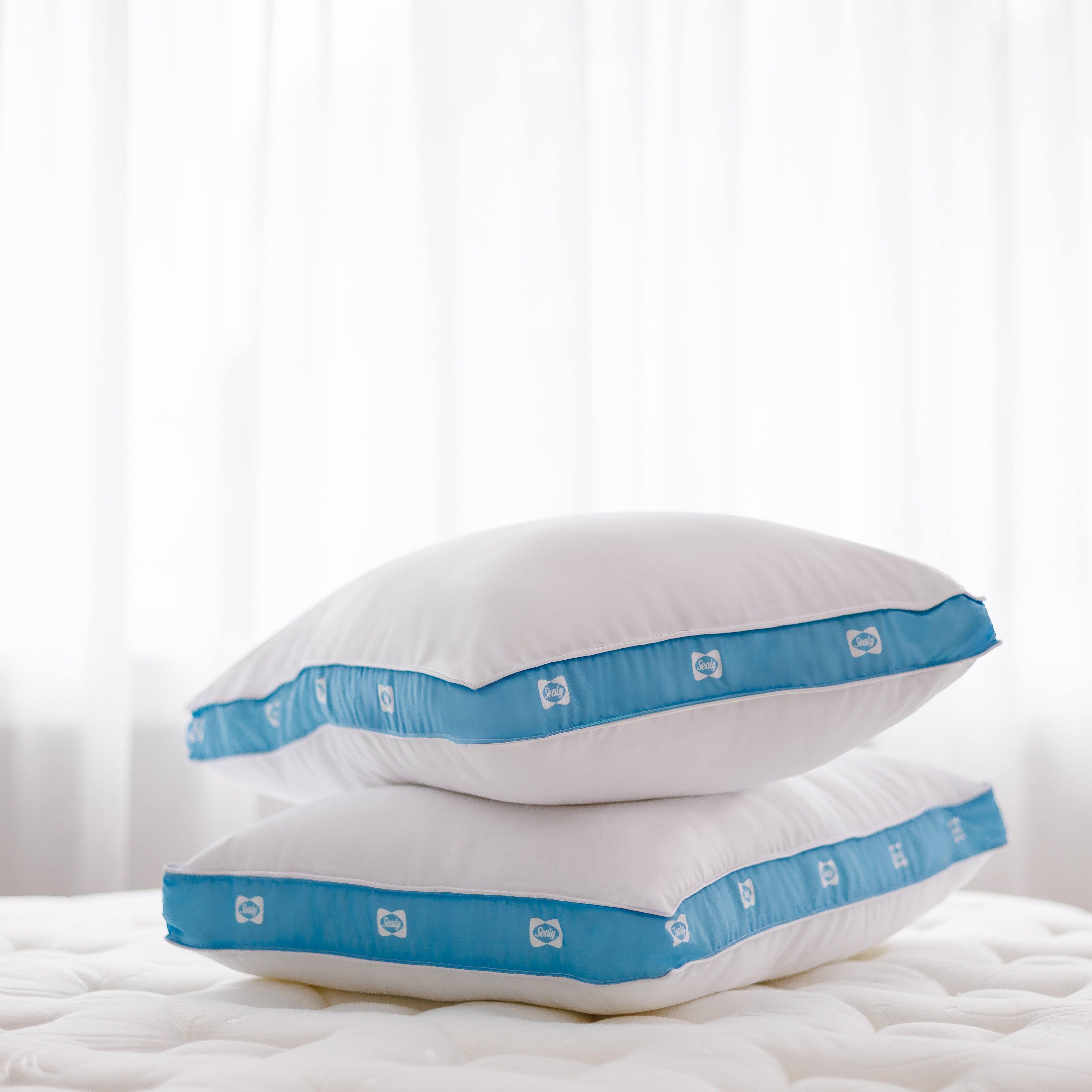 Two white pillows with blue bands on a white bedspread.