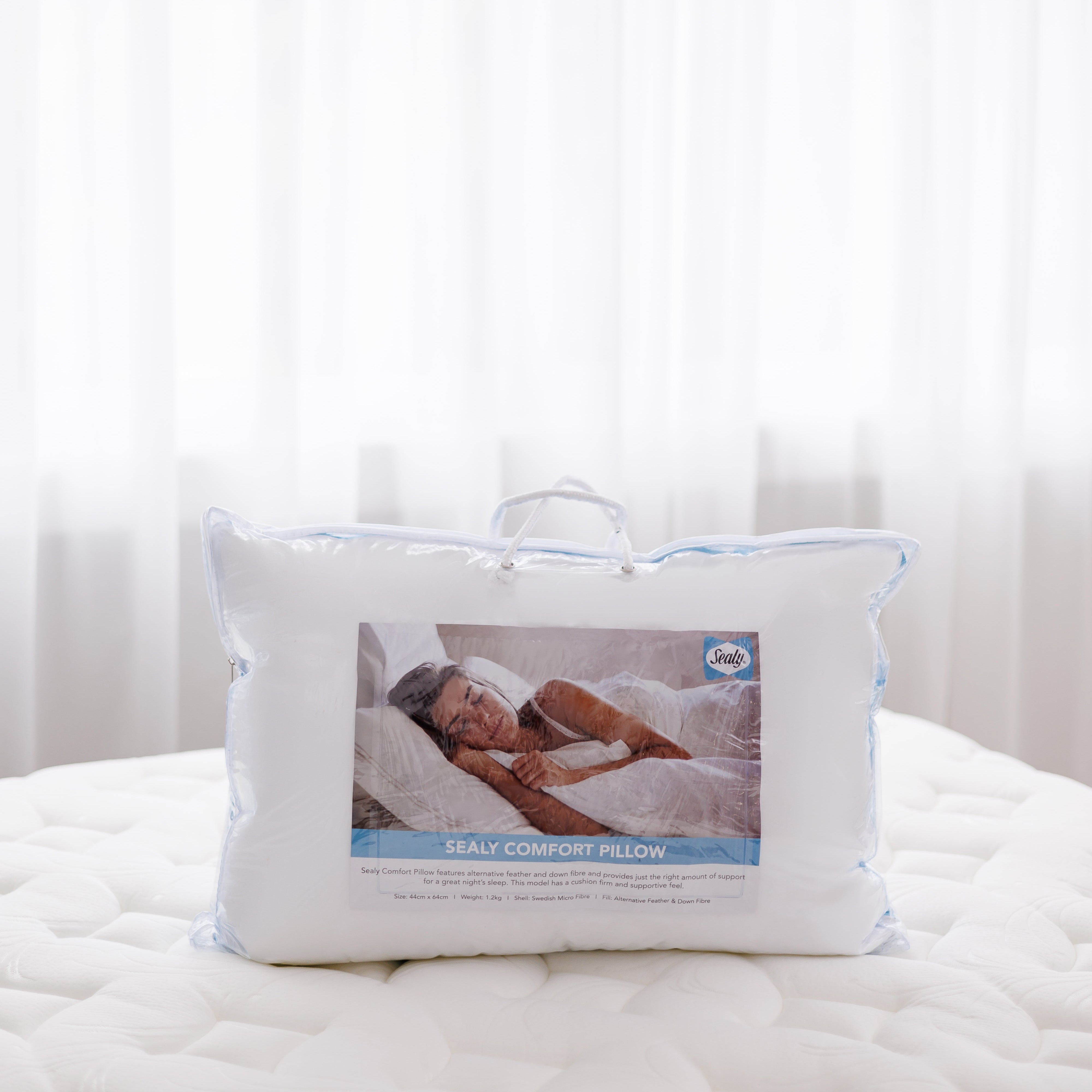 White pillow with a clear cover on a bed against a white curtain background